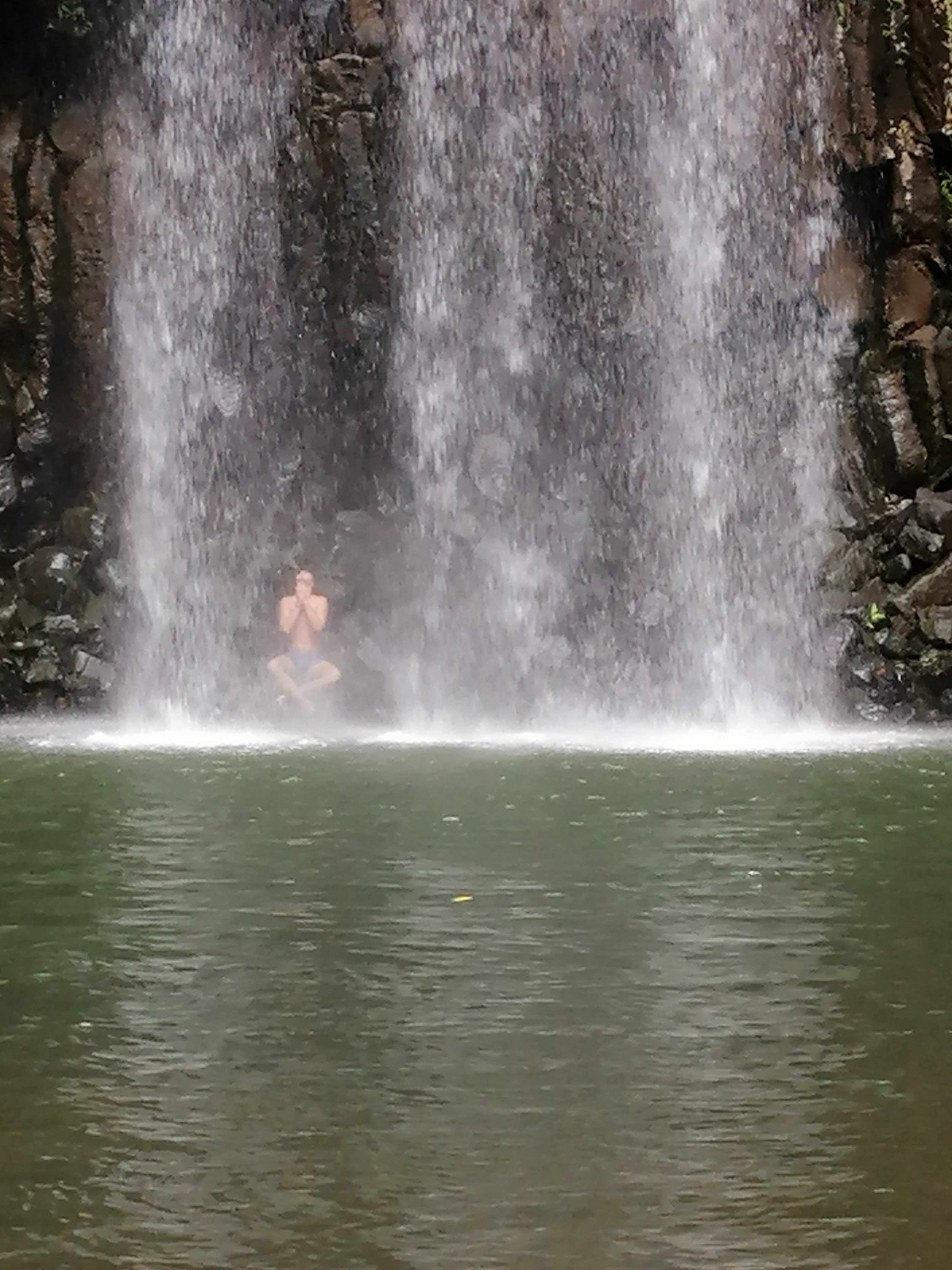 man sitting at the bottom of waterfall stream