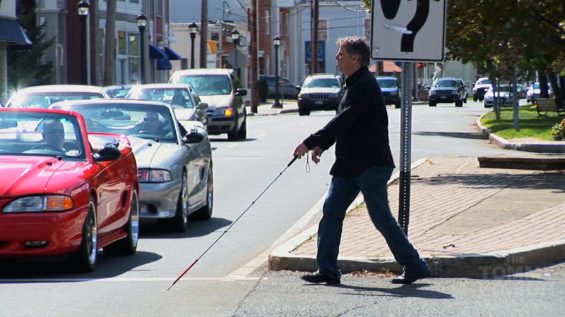 blind man walking across a road with his stick in front of him 